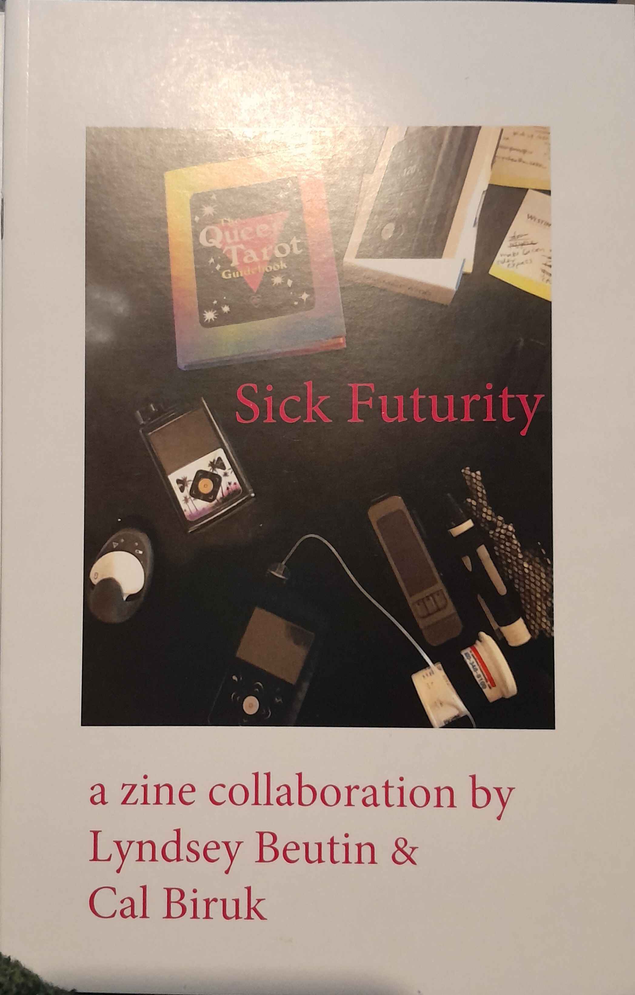 The title of the zine, "Sick Futurity", is written in a pink font set against a a photograph of the Queer Tarot Guidebook (by Ashley Molesso and Chess Needham) set out on a table with various diabetes measurement devices and notes. Below the photograph, the names of the authors, Lyndsey Beutin & Cal Biruk are written in the same pink font on a white background, which frames the photo.